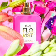 Florist 50ml Eau De Parfum with cap removed on pink background surrounded by pink, green, yellow, orange, and purple flowers.