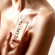 Model holding Myth 95ml Spectacular Scented Body Oil with out cap, near collarbone, on white background.