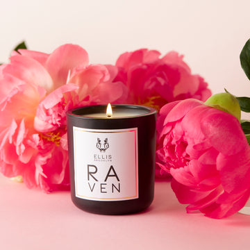Raven 6.5 oz. Terrific Scented Candle on light pink background with pink flowers.
