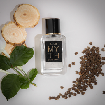 Myth 7.5ml Eau De Parfum Mini Dabber on white background with sandal wood, green leaves and ambrette seeds.