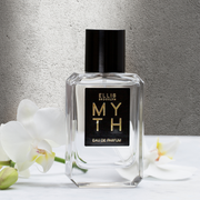 Myth 50ml Eau De Parfum on white table next to white flowers against grey wall.