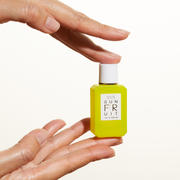 Model holding Sun Fruit 7.5ml Eau De Parfum Mini Dabber with fingertips of both hands, on white background.
