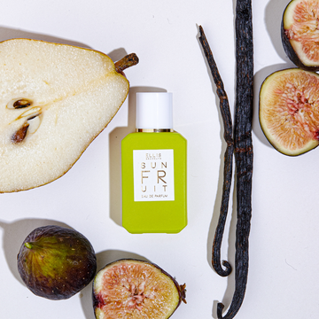 Sun Fruit 7.5ml Eau De Parfum Mini Dabber next to figs, vanilla beans, and pear, on white background.