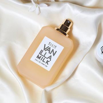 Vanilla Milk 50ml Eau De Parfum with cap removed on white satin sheet near white flower.